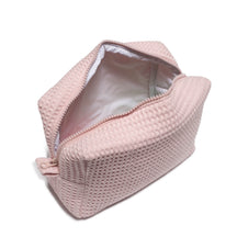 A light pink waffle zippered pouch or makeup bag is shown open, revealing a white inner lining. The bag has a rectangular shape and a woven-style exterior pattern.
