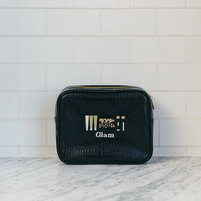 Black cosmetic bag with 'Glam' branding on a marble surface with white tiled wall background