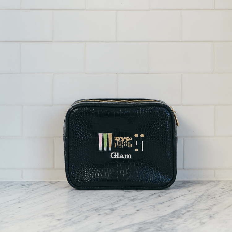Black cosmetic bag with 'Glam' branding on a marble surface with white tiled wall background