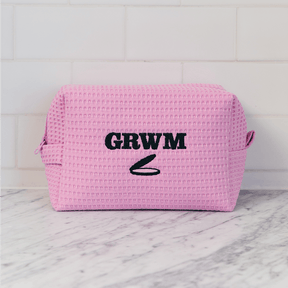 Pink woven pouch with 'GRWM' text on a marble surface