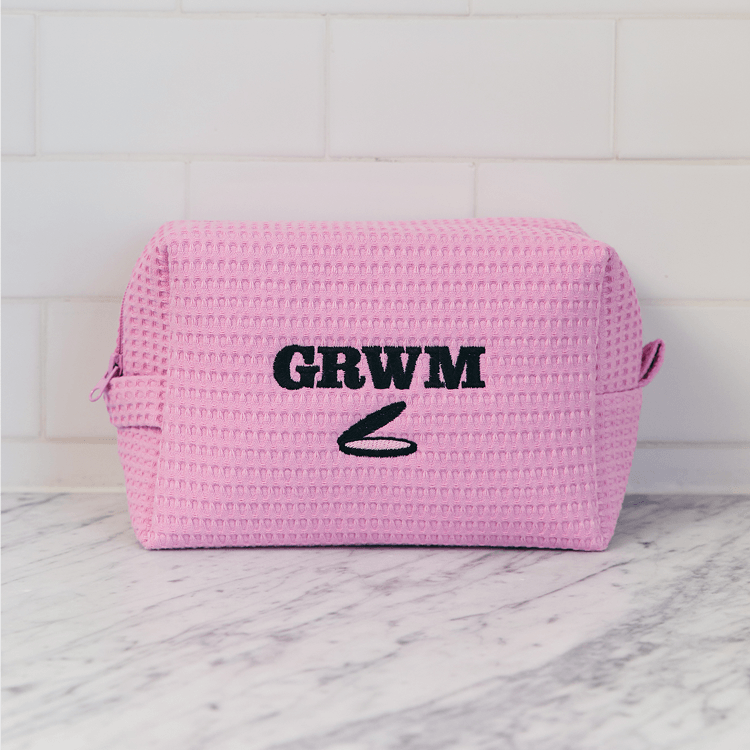 Pink woven pouch with 'GRWM' text on a marble surface