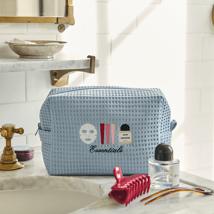 Blue waffle-textured cosmetic bag with 'essentials' text on a bathroom counter.