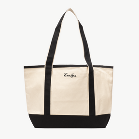 A beige canvas tote bag with long black handles and a matching black base. The name Evelyn is embroidered in black on the front, displayed on a white background.
