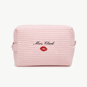 A light pink waffle pouch with the text 'Mrs. Clark' and a small embroidered kiss below on the front, displayed on a plain white background.