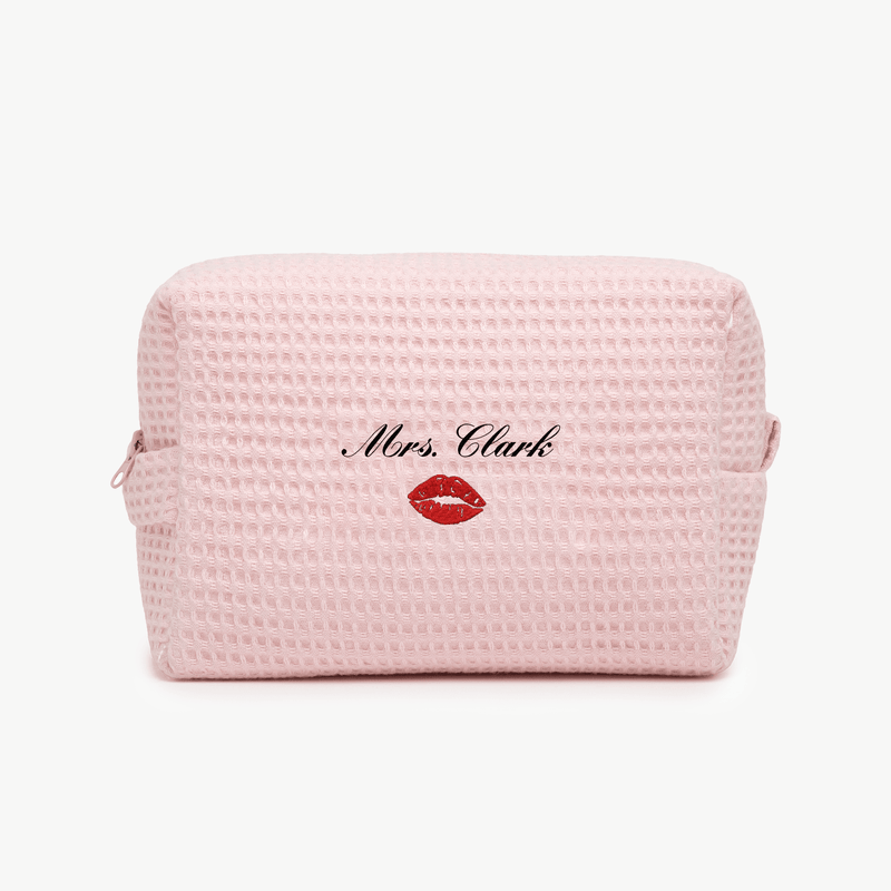 A light pink waffle pouch with the text 'Mrs. Clark' and a small embroidered kiss below on the front, displayed on a plain white background.