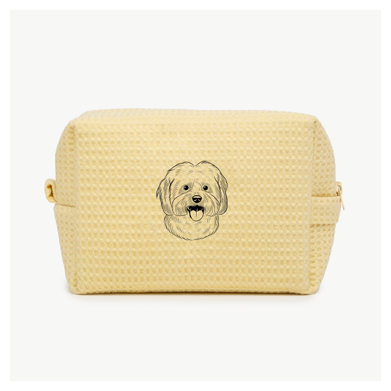 A light yellow waffle zippered pouch with a black line drawing of a dogs face on the front.