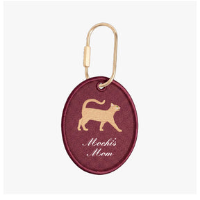 Maroon keychain with gold cat illustration and 'Mochi's Mom' text on a white background