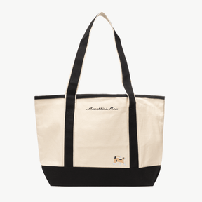 A beige canvas tote bag with long black handles and a matching black base the text 'Munchkin's Mom' near the top, and a small embroidered silhouette of a cat at the bottom right.