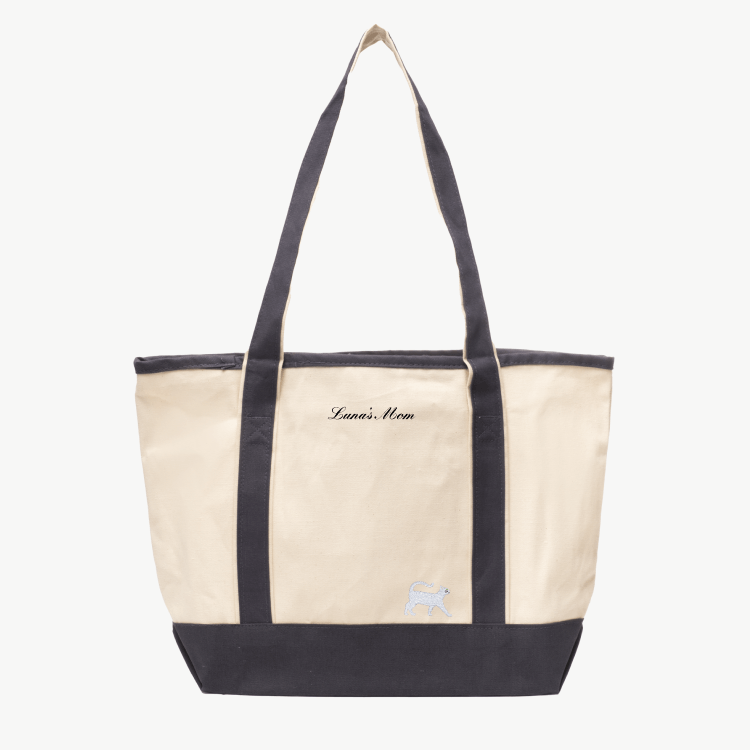 A beige canvas tote bag with long gray handles and a matching gray  base the text 'Luna's Mom' near the top, and a small embroidered silhouette of a cat at the bottom right.