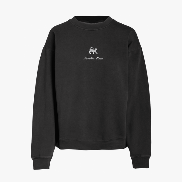 Black crewneck sweatshirt featuring a small embroidered gray cat above the words Mochi's Mom in white script on the chest. The sweatshirt has long sleeves and a simple, relaxed design.