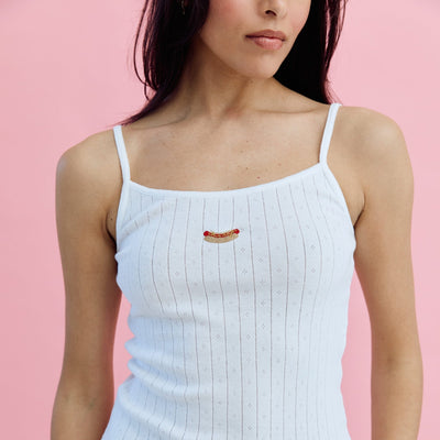Woman wearing a white ribbed tank top and blue jeans against a pink background