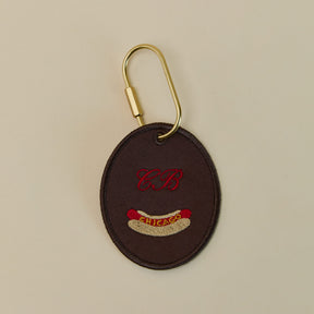 Brown keychain with embroidered design and gold clip on beige background
