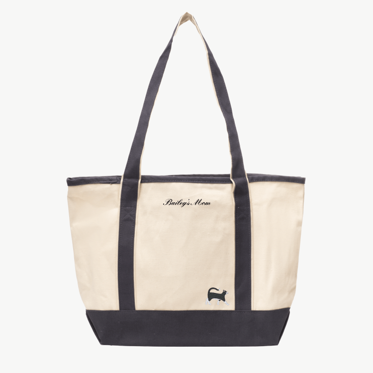 A beige canvas tote bag with long gray handles and a matching gray  base the text 'Bailey's Mom' near the top, and a small embroidered silhouette of a cat at the bottom right.