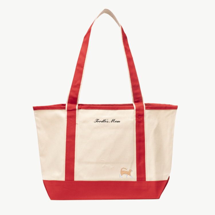 A beige canvas tote bag with long red handles and a matching red base the text 'Toodle's Mom' near the top, and a small embroidered silhouette of a cat at the bottom right.