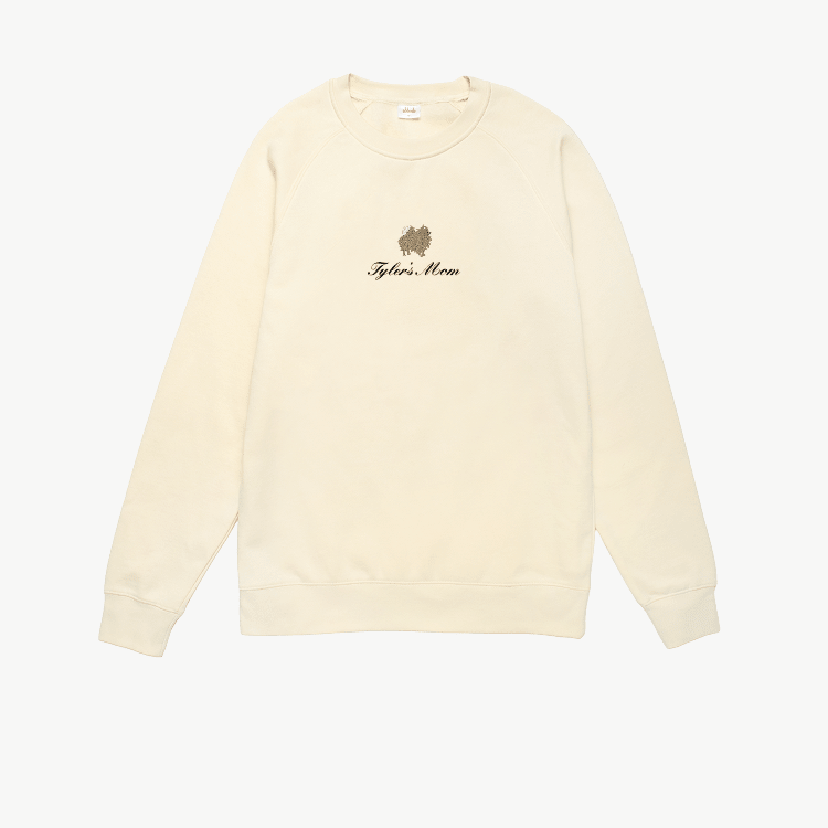 Cream crewneck sweatshirt featuring a small embroidered brown dog above the words Tyler's Mom in black script on the chest. The sweatshirt has long sleeves and a simple, relaxed design.