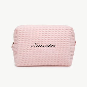 A light pink waffle pouch with the word Necessities written in elegant black script on the front.