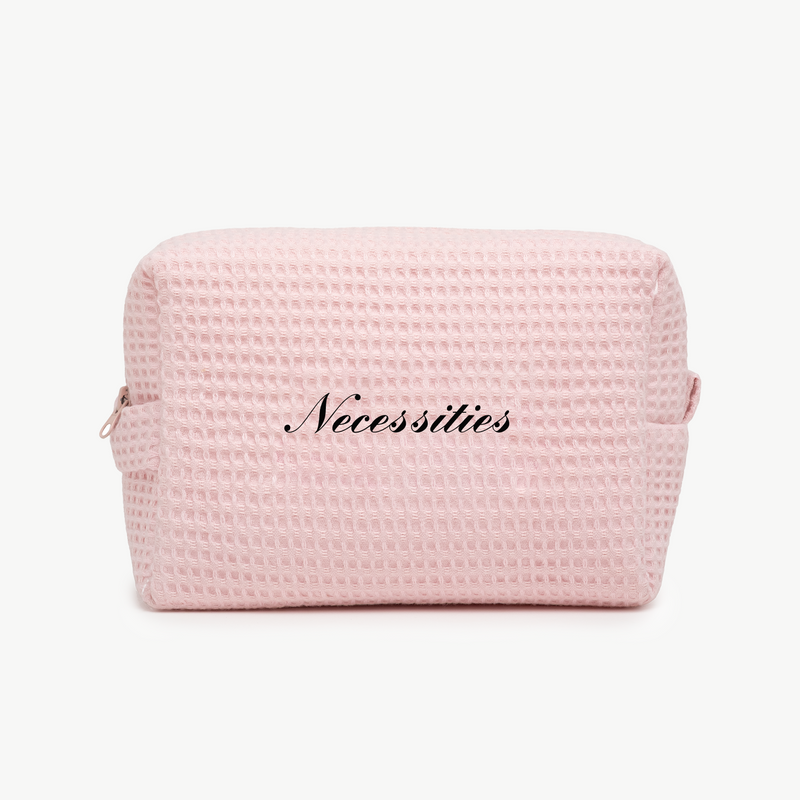 A light pink waffle pouch with the word Necessities written in elegant black script on the front.