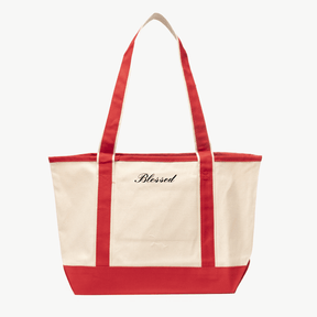 A beige canvas tote bag with red handles and a matching red base. The words Blessed are embroidered in red script on the front above the pocket. The background is plain white.