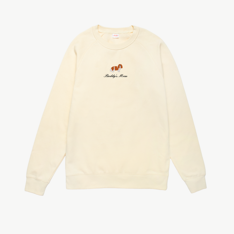 Cream crewneck sweatshirt featuring a small embroidered brown dog above the words Buddy's Mom in black script on the chest. The sweatshirt has long sleeves and a simple, relaxed design.