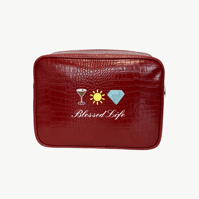 A red faux-croc pouch features icons of  a martini glass, sun, and diamond above the words Blessed Life in cursive white text.