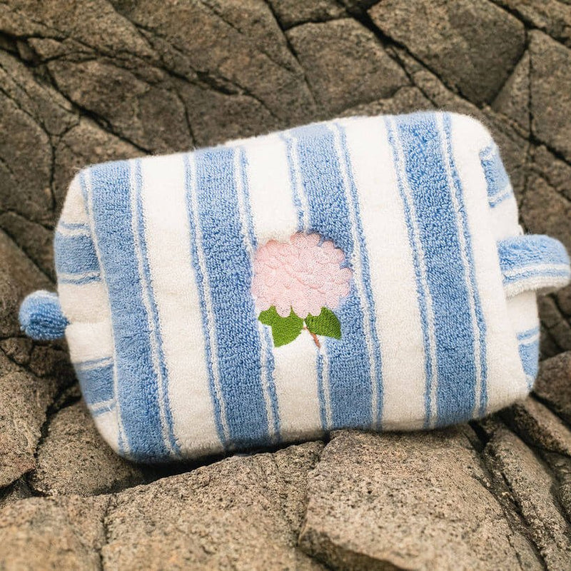 Blue and white striped pouch with a floral design on a rocky surface