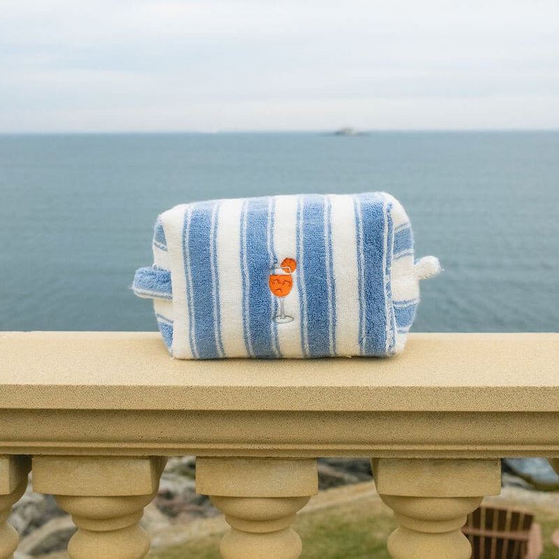 Blue and white striped pouch on a stone ledge by the ocean.