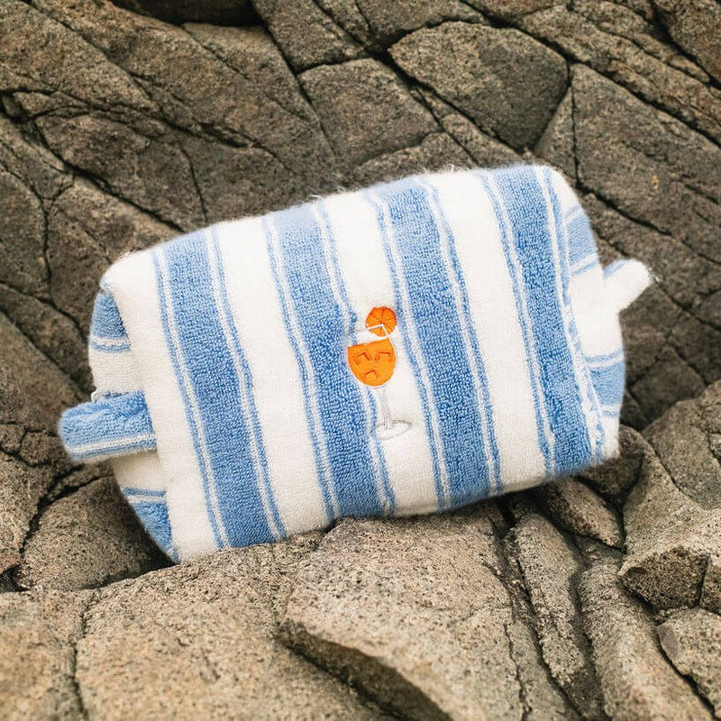 Blue and white striped pouch with a small orange character on a rocky surface