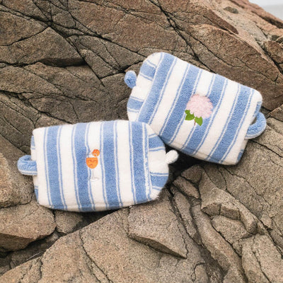 Pair of blue and white striped pouches with embroidered designs on a stone surface