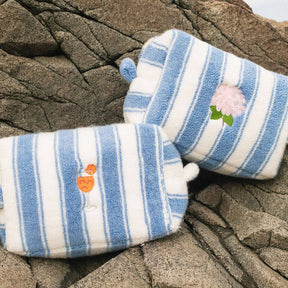 Pair of blue and white striped pouch with floral and drink designs on a rocky surface.