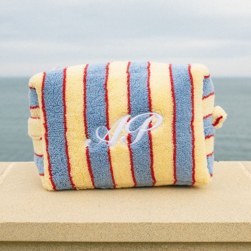 Striped pouch with initials on a wooden surface by the ocean