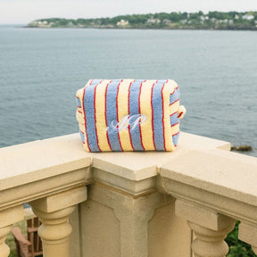 Striped bag with a monogram on a stone ledge overlooking a body of water.