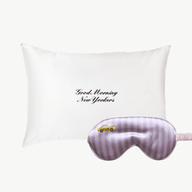White pillow with 'Good Morning New Yorkers' text and a pink striped eye mask
