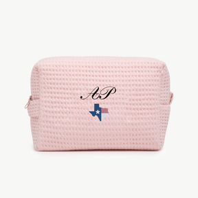 A light pink, waffle pouch with the initials AP and a small embroidered state of Texas with colored as Texas flag  below the name on the front.