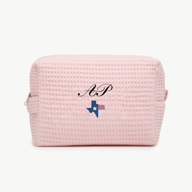A light pink, waffle pouch with the initials AP and a small embroidered state of Texas with colored as Texas flag  below the name on the front.