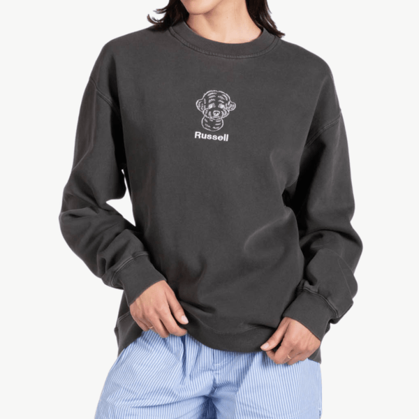 A person wearing a loose-fitting black sweatshirt with a line art dog face and the word Russell on the chest, paired with light blue striped pants.