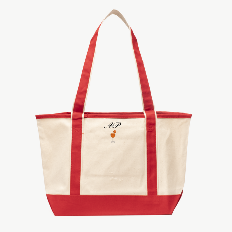 A beige canvas tote bag with long red handles and a matching red  base, featuring 'A&P' and an Aperol Spritz icon embroidered on the front, displayed on a white background.