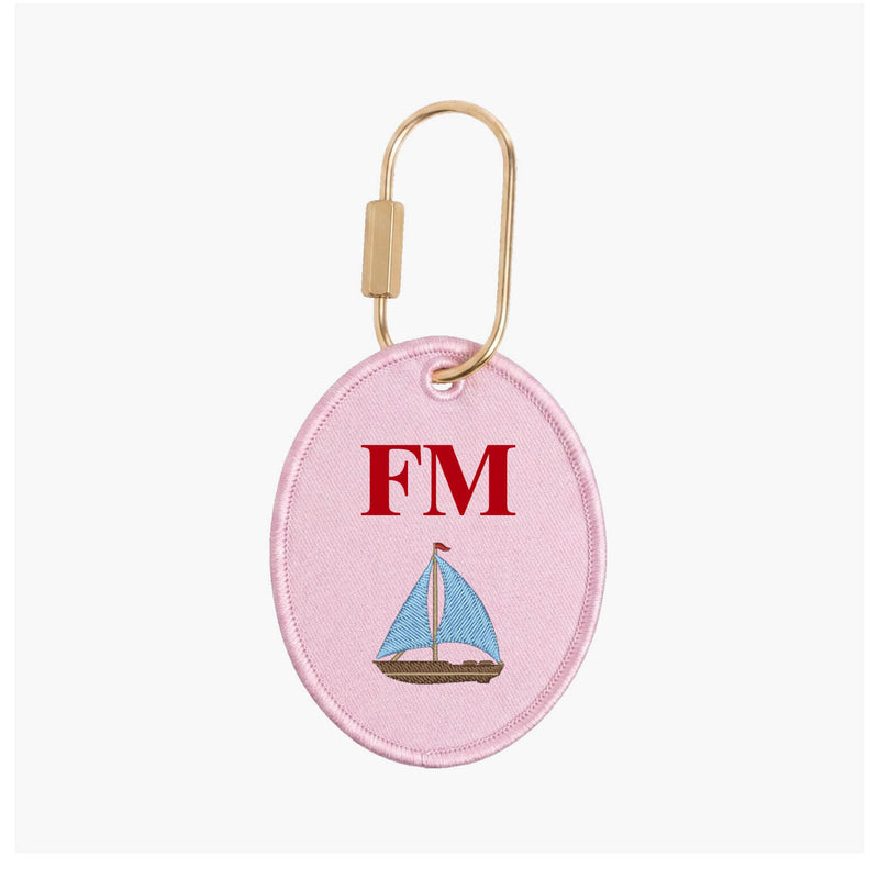 Pink oval keychain with sailboat design and 'FM' initials on a white background