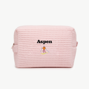 A light pink waffle pouch with the text 'Aspen' and an embroidered skier below the name on the front.