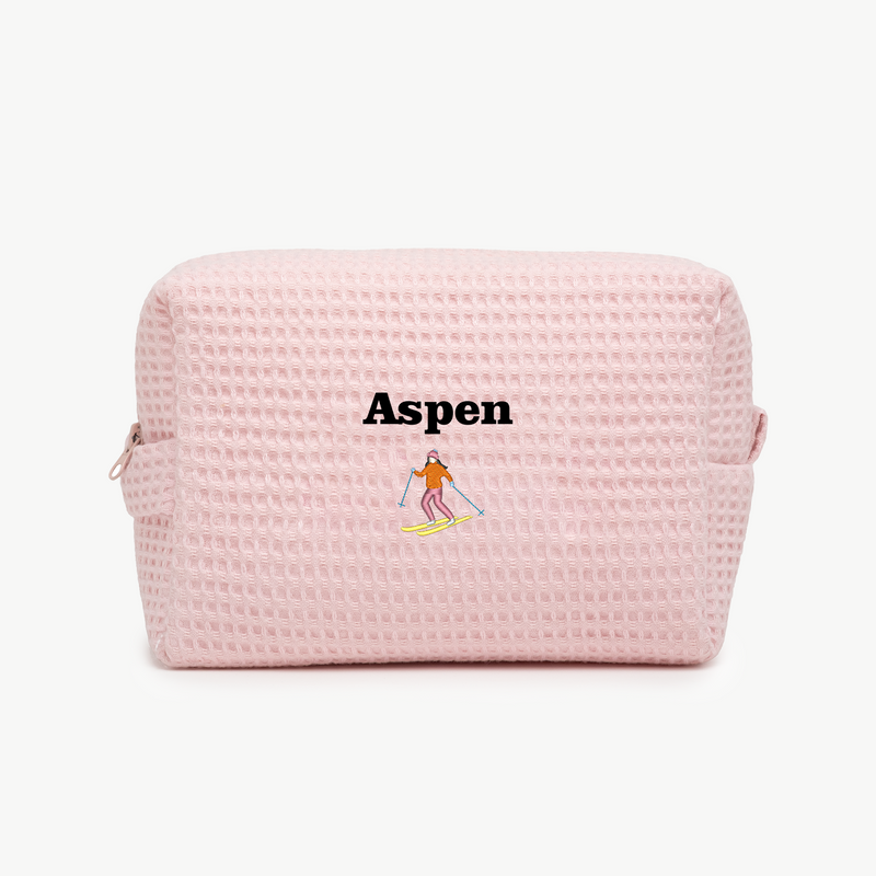 A light pink waffle pouch with the text 'Aspen' and an embroidered skier below the name on the front.