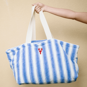 Blue and white striped tote bag with a lobster logo held by a person against a beige background