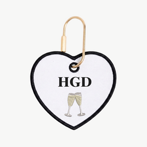 Heart-shaped keychain with 'HGD' and champagne glass design on a white background
