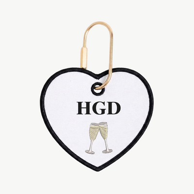 Heart-shaped keychain with 'HGD' and champagne glass design on a white background