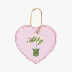 Heart-shaped keychain with 'Abby' and a green drink design on a white background