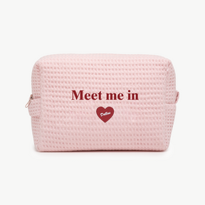 Pink textured pouch with 'Meet me in Dallas' text on a white background
