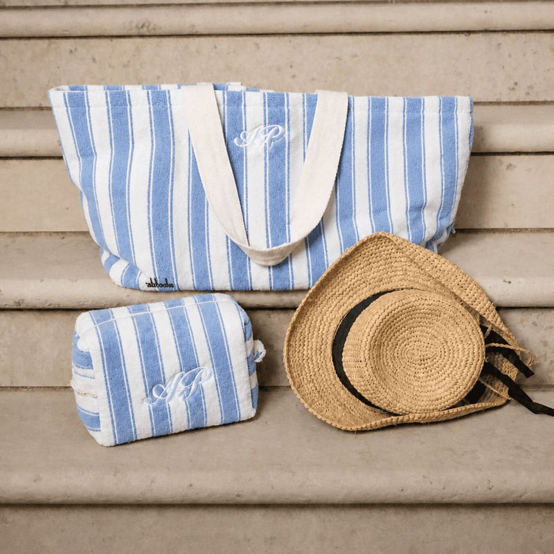 Blue and white striped bag and pouch with a straw hat on a wooden surface