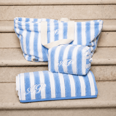 Blue and white striped tote bag, pouch and towel with monograms on a wooden surface