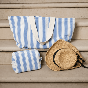 Blue and white striped beach bag and towel with a straw hat on a wooden surface