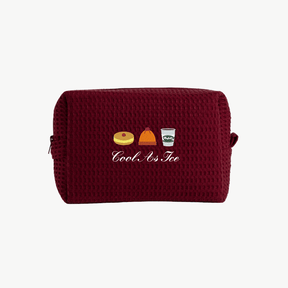A maroon waffle pouch with embroidered images of a pie, a beanie hat, and a coffee, along with the words Cool As Ice beneath the images.