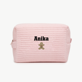 A light pink, waffle zippered pouch with the name Anika and an embroidered gingerbread man below the name on the front.