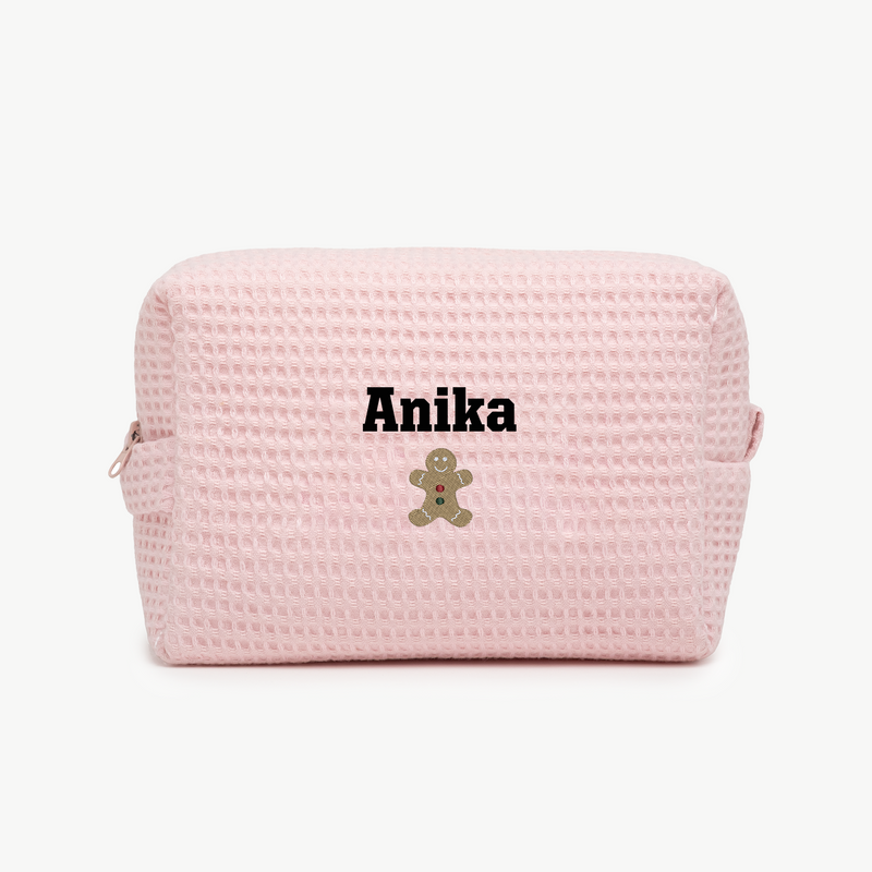 A light pink, waffle zippered pouch with the name Anika and an embroidered gingerbread man below the name on the front.
